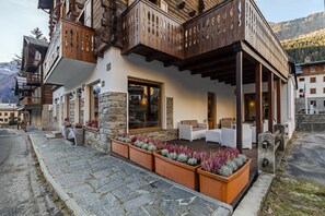 A hotel with a stone facade, wooden balconies, outdoor seating, and a mountain backdrop. - Hotel Dufour (Macugnaga)