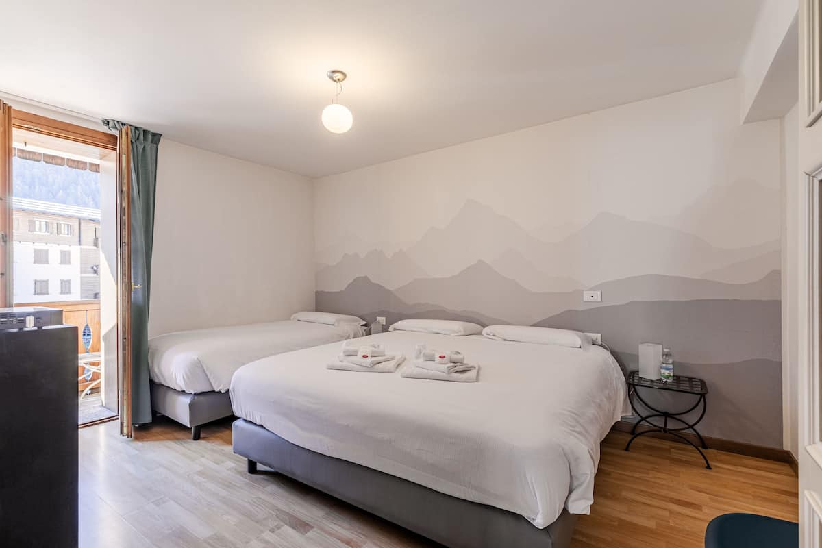 Une chambre d’hôtel avec deux lits, une petite table sur laquelle se trouve une bouteille, et une vue sur les montagnes par la fenêtre.