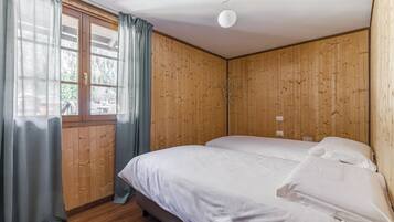 Una habitación con paneles de madera, una cama con ropa de cama blanca, una ventana con cortinas y una lámpara de techo.