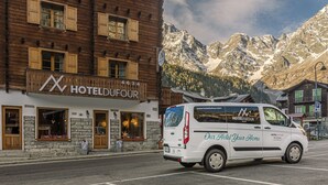 A white van with "HOTELDUFOUR" and "Our Hotel Your Home" on the side parked in front of a wooden building with a sign that reads "HOTELDUFOUR". - Hotel Dufour (Macugnaga)