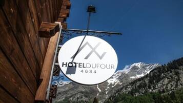 A wooden building with a sign that reads "HOTELDUFOUR 4634" against a backdrop of snow-capped mountains.