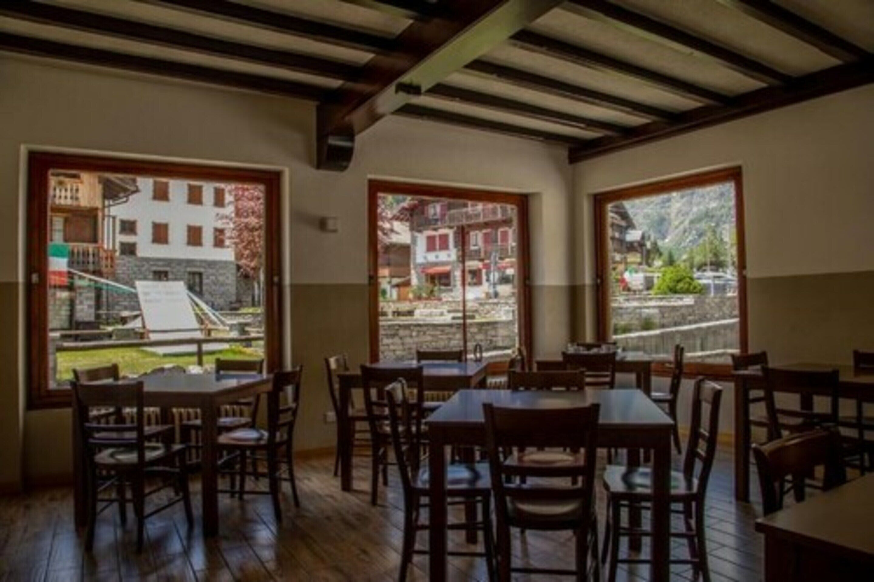 A dining area with wooden tables and chairs, large windows with views of buildings and a garden.
