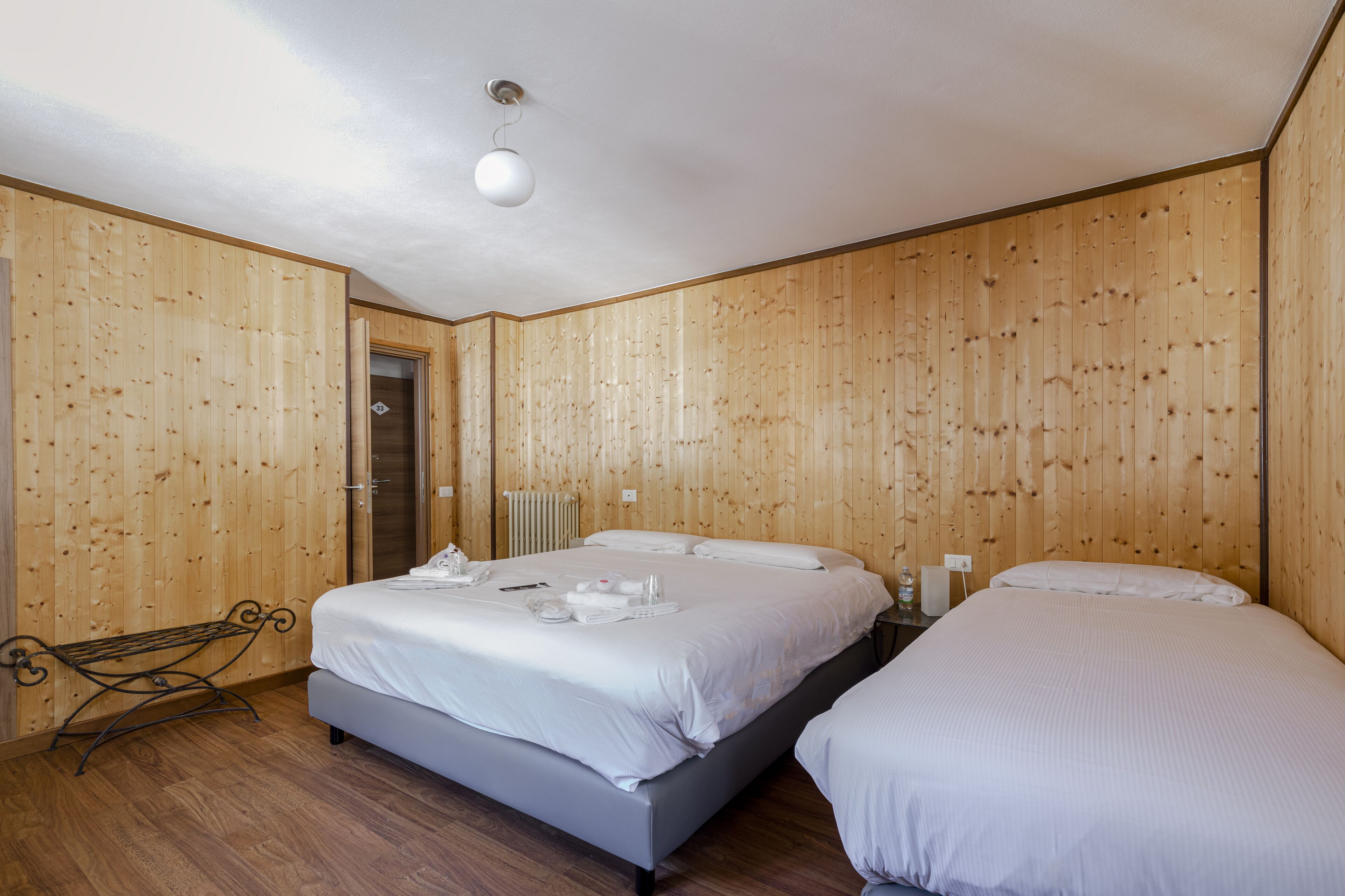 A room with wooden panel walls, a bed with white linens, a bedside table, and a hanging light fixture.
