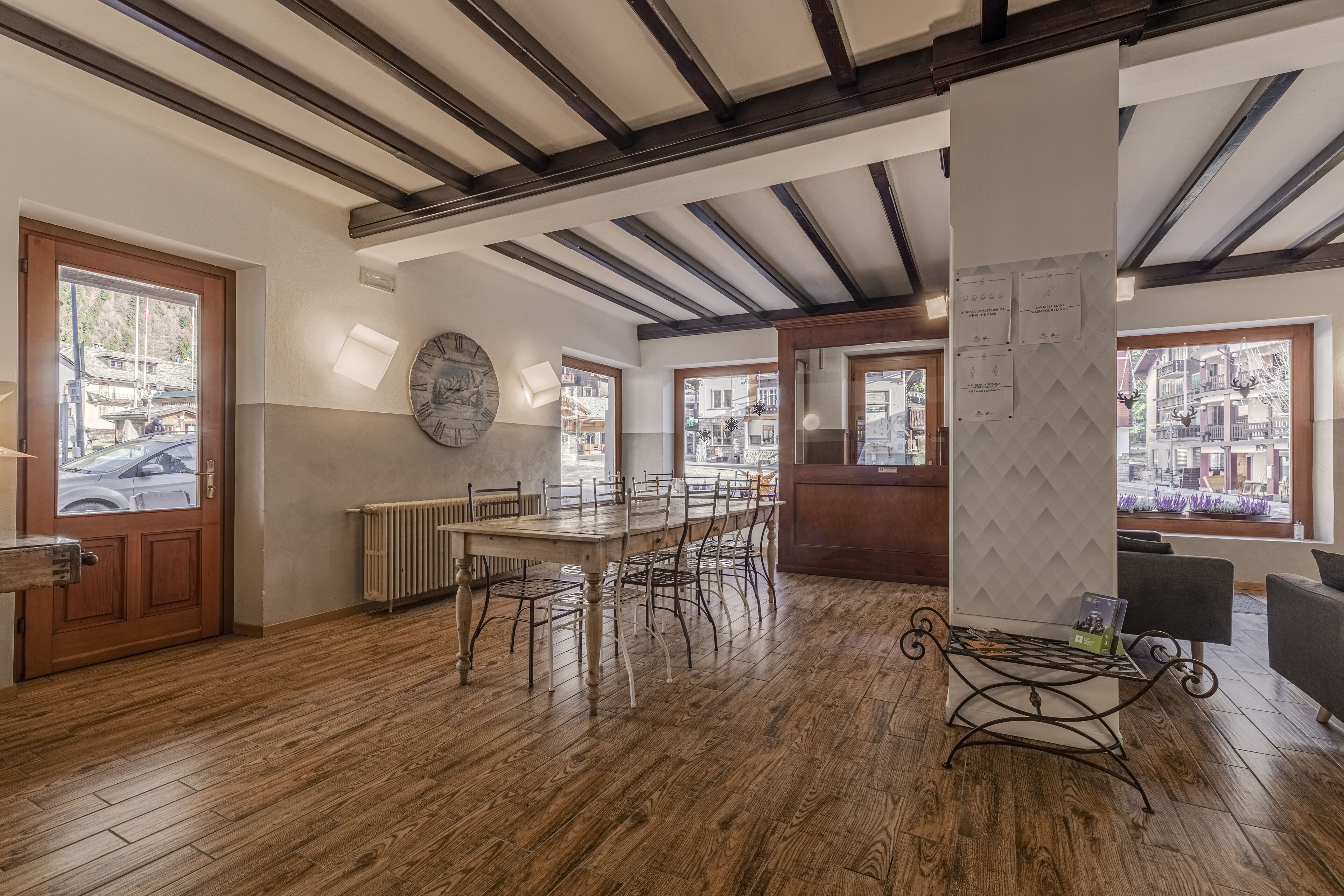 Una habitación amplia con piso de madera, una gran mesa de comedor y sillas. Hay un radiador, un reloj y una ventana con vistas a edificios.