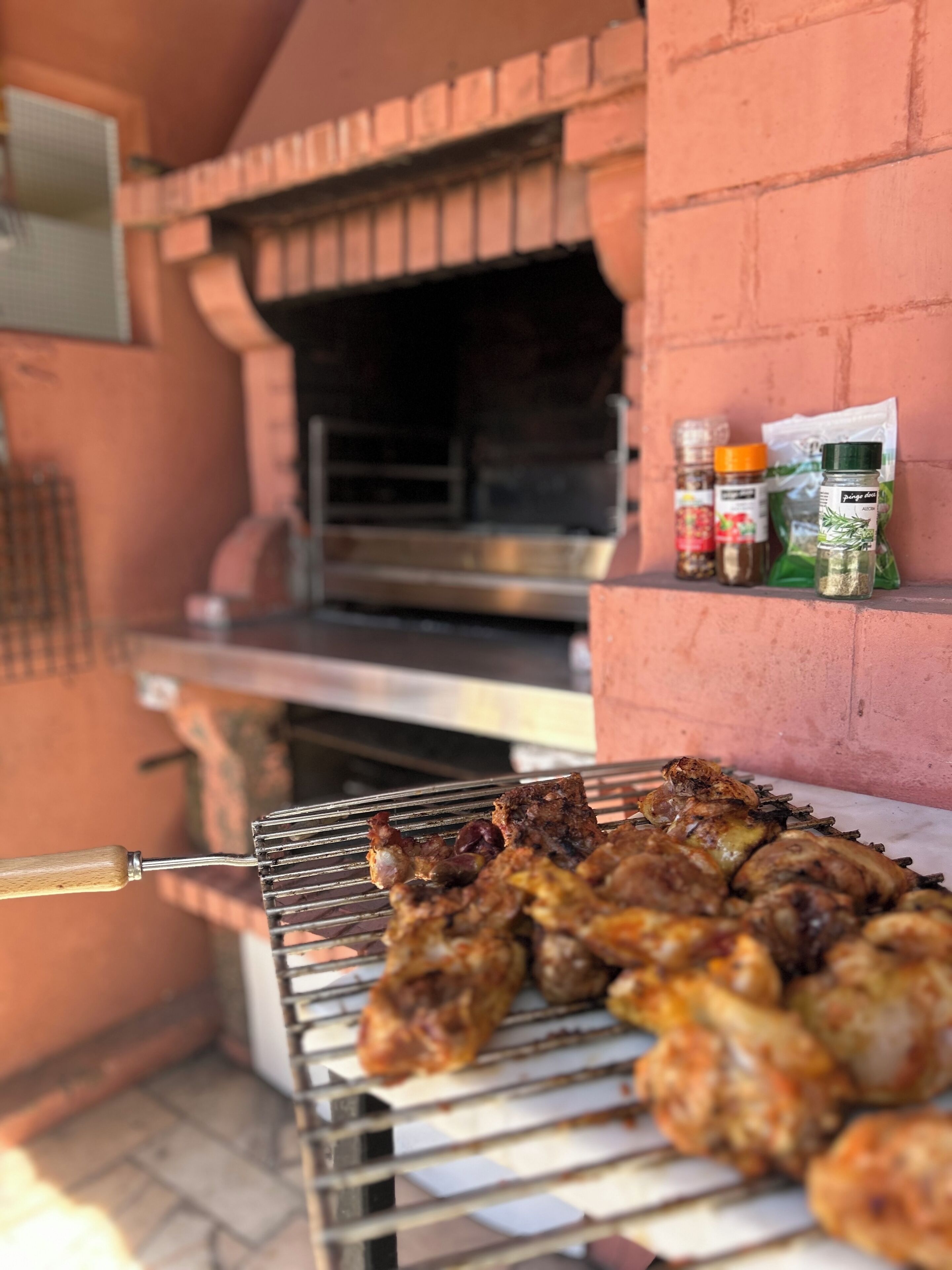 Ein Backstein-Grill mit verschiedenen Fleischsorten, die gegrillt werden, und ein Gemüserostern in der Nähe.