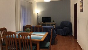 En matplats med ett träbord och stolar, en tv på ett stativ och en blå soffa.