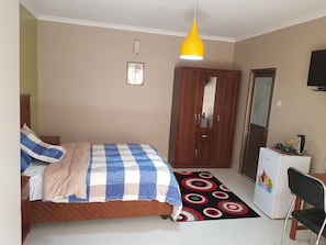 Quarto com cama, guarda-roupa, escrivaninha, cadeira, frigorífico e televisão.