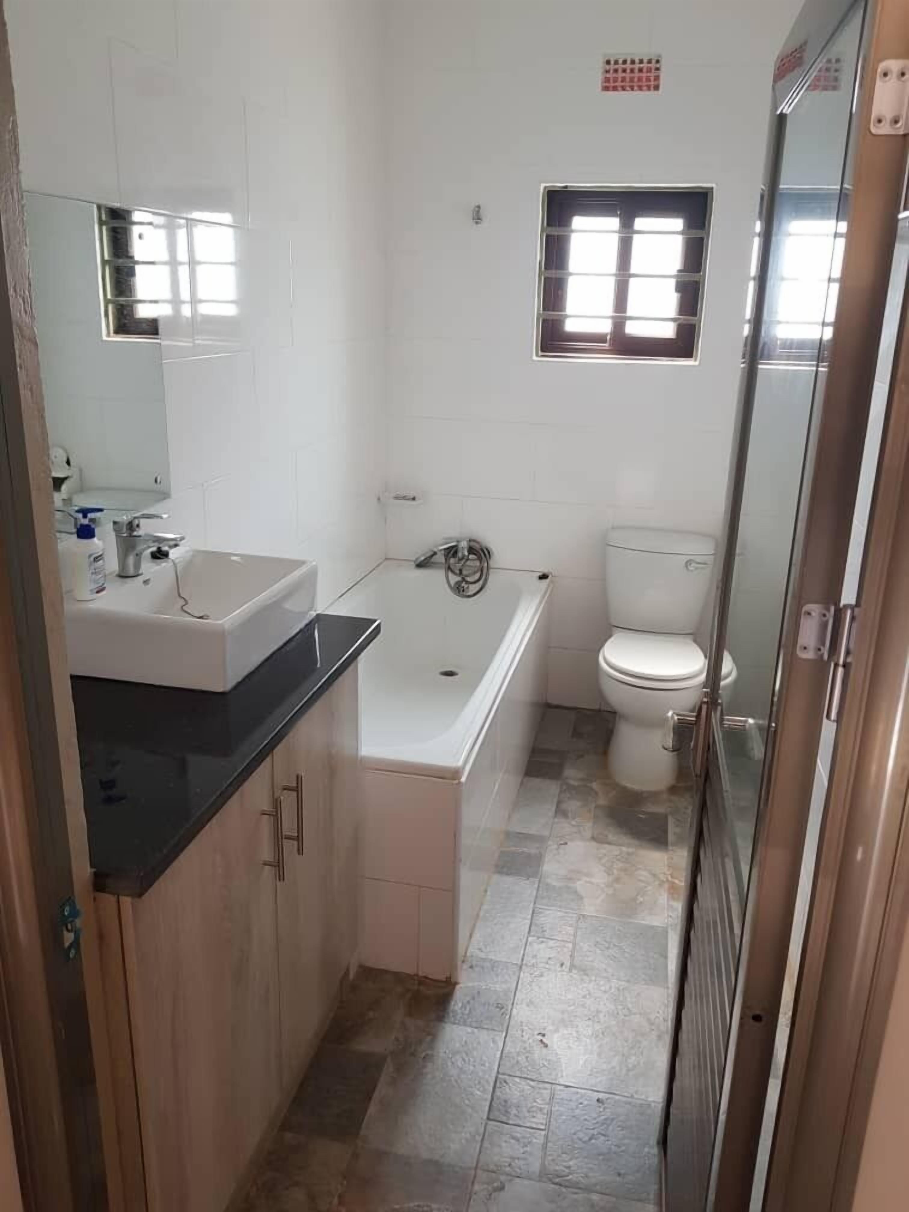 Un baño con lavamanos, bañera, inodoro y un ventanal pequeño.