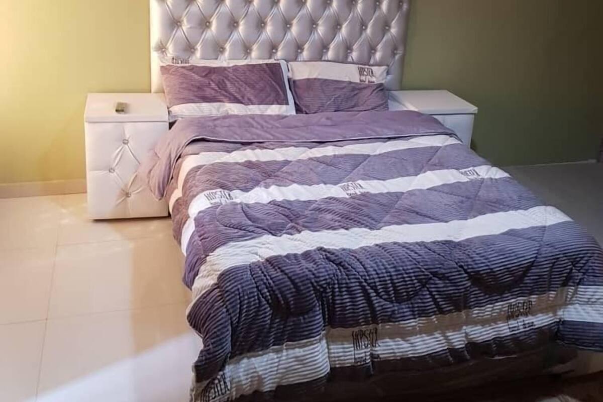Un dormitorio con cabecera capitonada, edredón a rayas y alfombra estampada.