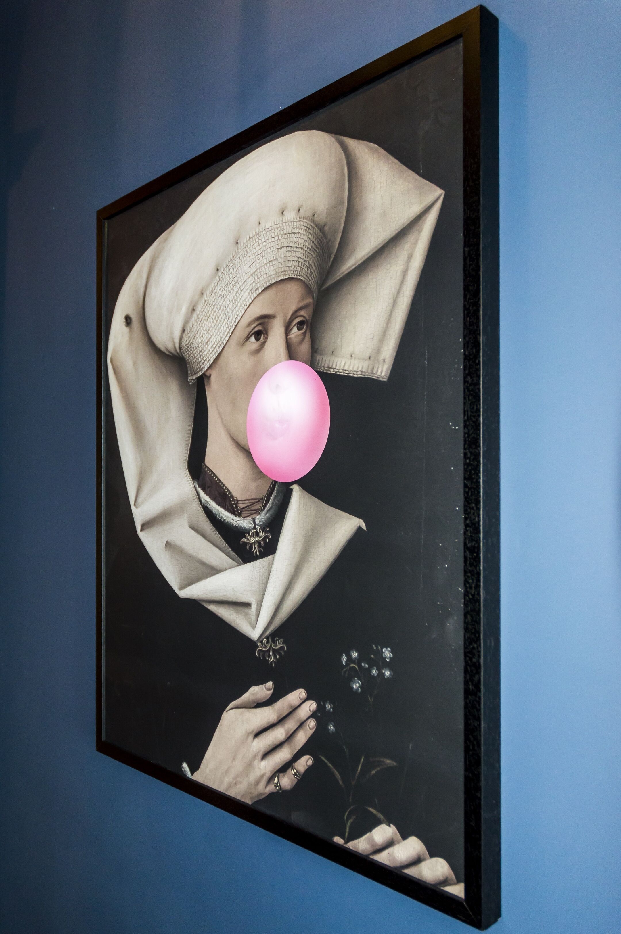Une œuvre d’art encadrée représentant une personne portant un couvre-chef, tenant un ballon rose et une fleur dans la main.