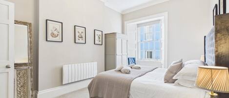 A bedroom with a bed, a radiator, a wardrobe, a window, and framed pictures on the wall.