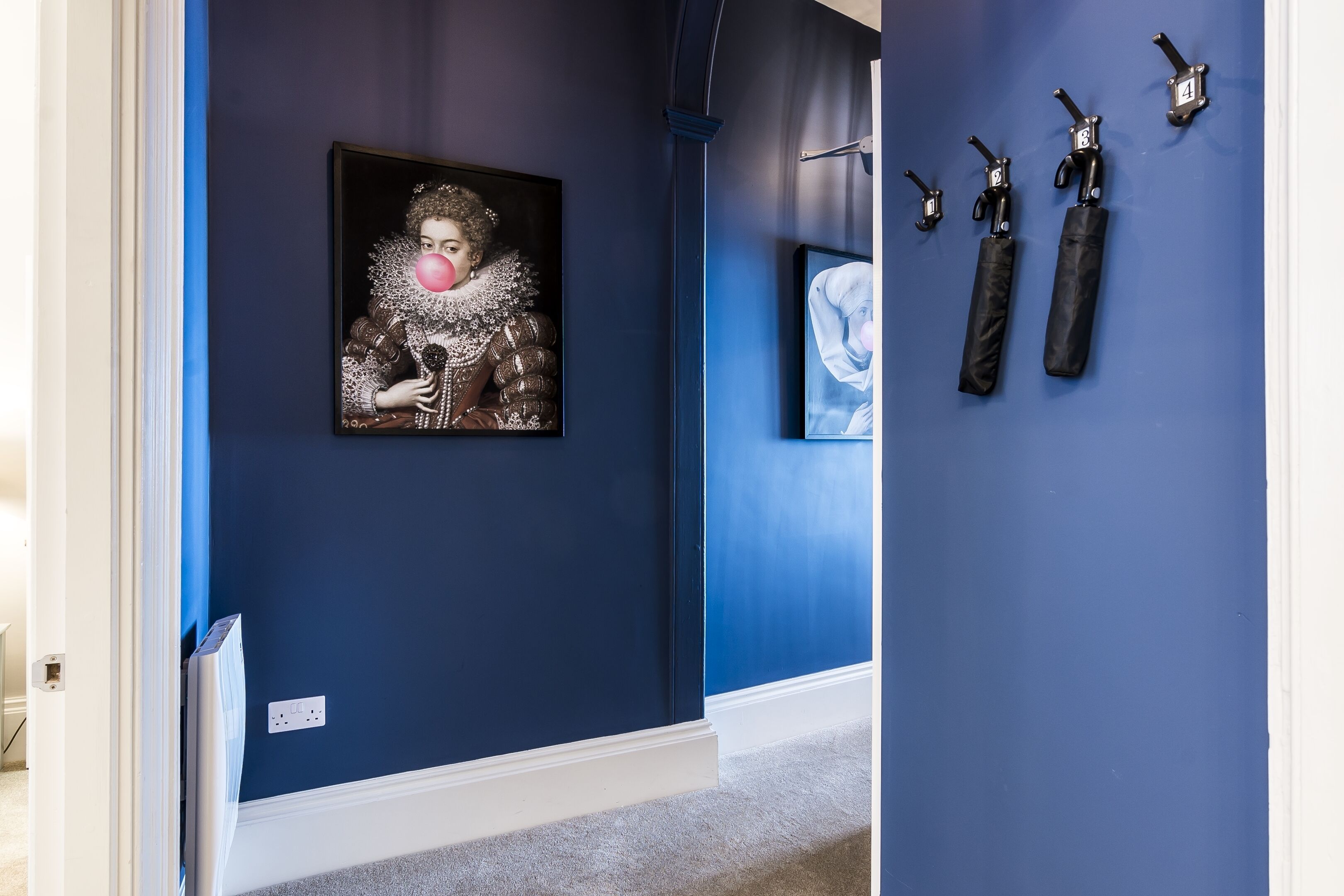 A hallway with a blue wall, a framed artwork, and a set of black umbrellas mounted on the wall.