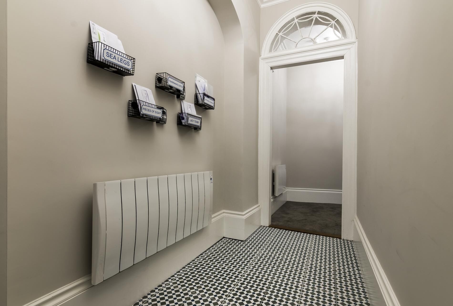 A hallway with a radiator, a checkered floor, and wall-mounted storage units labeled "SEA LEGS," "PIECES OF EIGHT," and "LADY TENNY."
