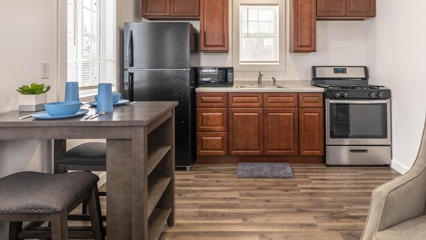 A kitchen with wooden cabinets, a black refrigerator, a microwave, a stove, and a sink.