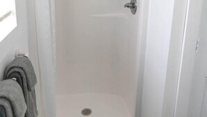 A white shower enclosure with a drain, a door, and a towel rack with a folded towel.