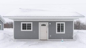 A two-story house with a gray exterior and white trim around the windows and door. - Sparkling Clean! 2 Bedroom Cottage- Located in Beautiful Keweenaw (Calumet)