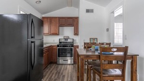 A kitchen with wooden cabinets, a black refrigerator, a stove, and a dining table with chairs. - Sparkling Clean! 2 Bedroom Cottage- Located in Beautiful Keweenaw (Calumet)