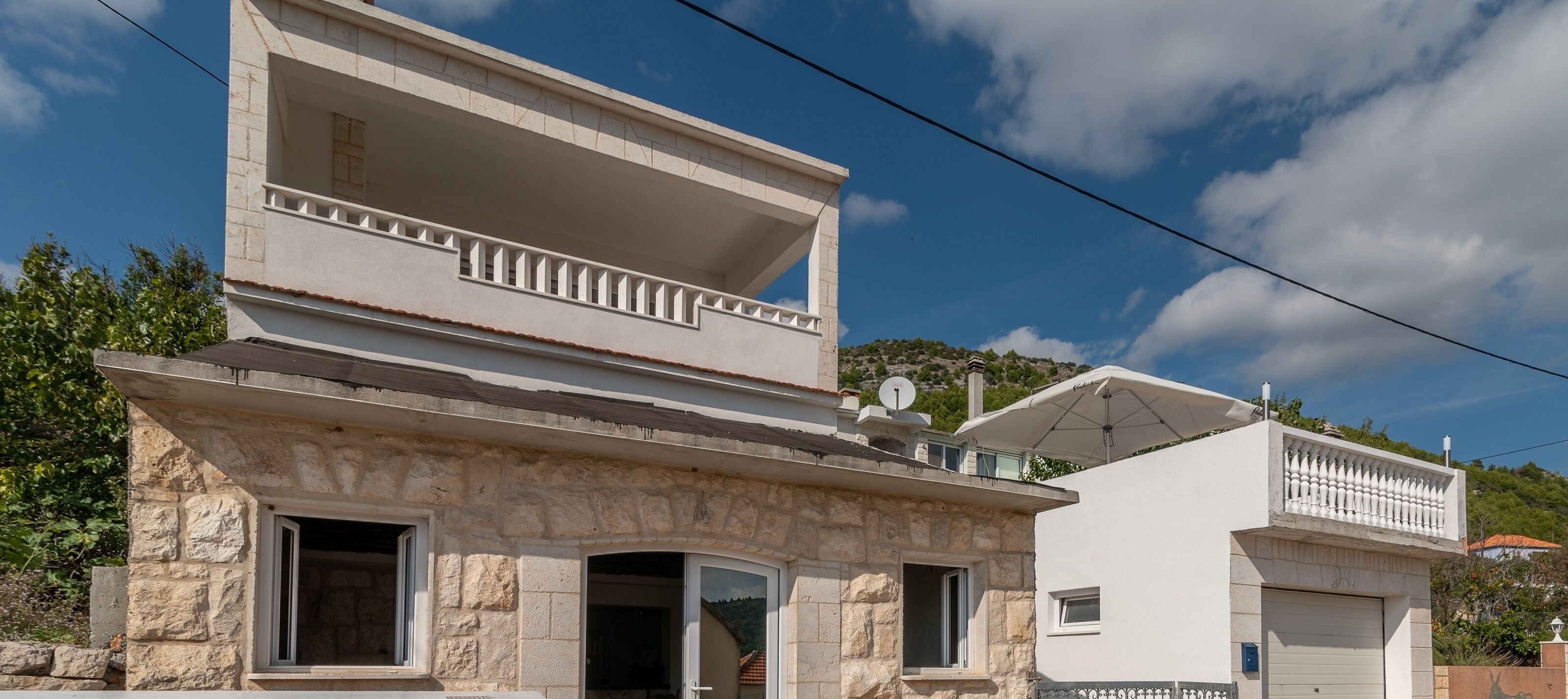 A two-story building with a stone facade, a balcony on the upper floor, and a satellite dish on the roof.