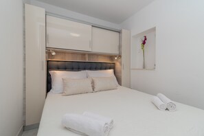 A neatly made bed with white linens, a headboard with built-in lighting, and a small vase with flowers on the wall. - Eden Mediterranean house (Marina)