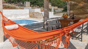 A hammock by a pool with a table and chairs, surrounded by stone walls and greenery. - Eden Mediterranean house (Marina)
