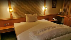 Una habitación de hotel con una cama grande, dos mesitas de noche, una lámpara y un teléfono.