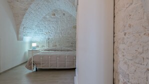 Un dormitorio con pared de piedra, cama, mesita de noche y lámpara.