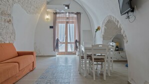 Una habitación con un sofá blanco, una mesa de comedor con sillas y un televisor montado en la pared.