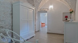 Una habitación con un armario blanco, una cama con cabecera blanca y una lámpara roja sobre una mesita.