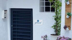 A building with a closed black door, a small window with a sign reading "giuacasud", and potted plants on the right side. - Giùasud (Ostuni)
