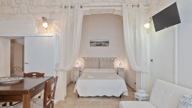 Een slaapkamer met een bed, een witte bank, een houten tafel en een aan de muur bevestigde televisie.