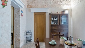 Un comedor con una mesa de madera, sillas, un mueble con puertas de vidrio y una cafetera.