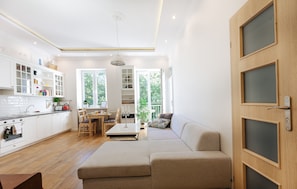 Una cocina moderna con armarios blancos, un comedor con mesa y sillas, y un amplio ventanal con vistas a la vegetación exterior.