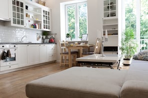 Uma cozinha moderna com armários brancos, uma área de refeições com mesa e cadeiras, e uma janela grande que oferece luz natural.