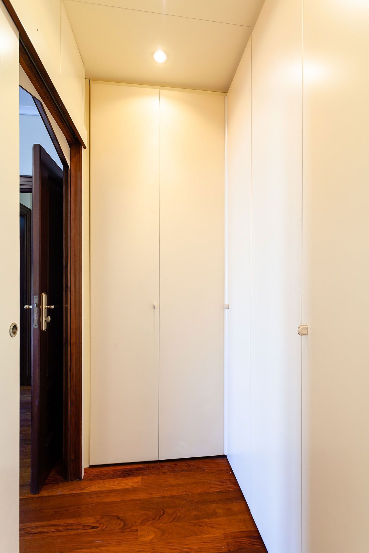 A hallway with wooden flooring leading to a set of white double doors.