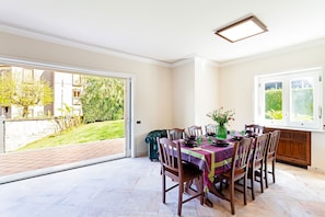 Un comedor con una mesa dispuesta para cuatro personas, un jarrón de flores y vistas a un jardín por un ventanal corredero.