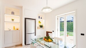 Una cocina moderna con armarios blancos, un refrigerador empotrado y una mesa de vidrio con un cuenco de fruta.