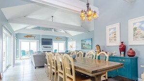 A spacious dining area with a large wooden table and chairs, a teal-colored cabinet, and a chandelier.