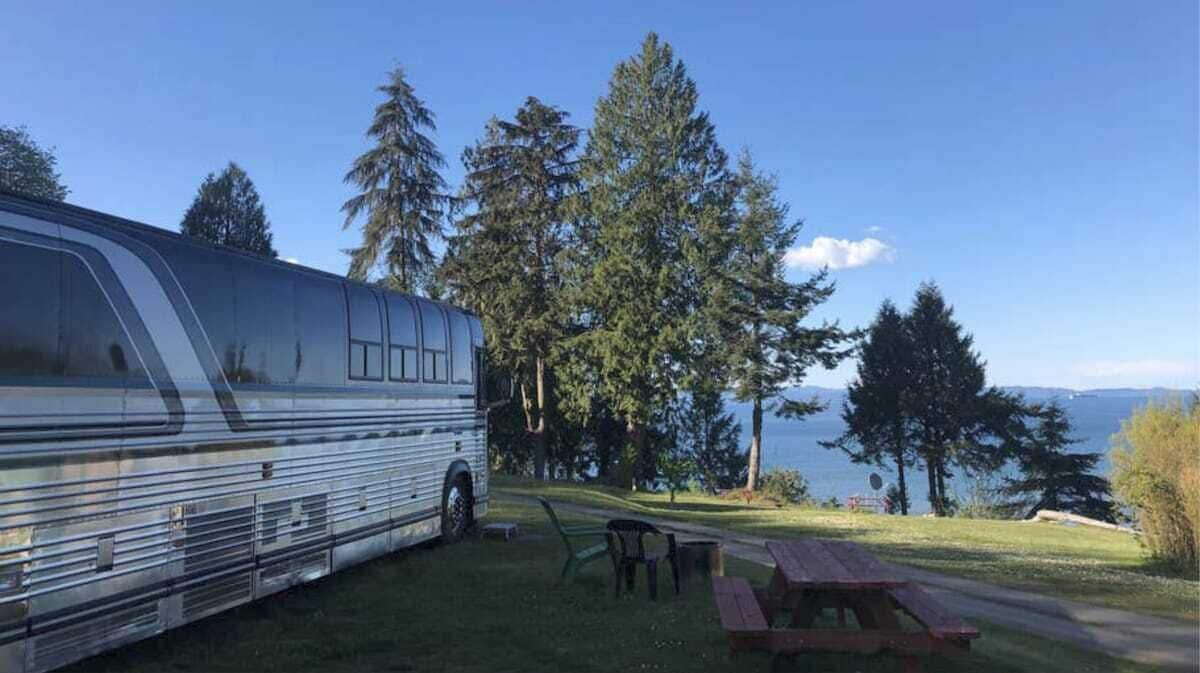 Ein Wohnmobil am Seeufer mit Picknicktischen und Stühlen.