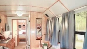 Un intérieur de camping-car accueillant, avec un canapé en cuir rouge, une petite table et un coin cuisine visible à travers une porte ouverte.