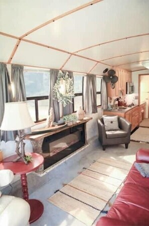 Un interior acogedor con un sofá rojo, una mesita redonda y una silla. Se ve una zona de cocina con armarios y un fregadero al fondo.