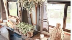 Une pièce chaleureuse avec une cheminée, une grande fenêtre avec des rideaux et une décoration rustique comprenant un panier tressé et une plante en pot.