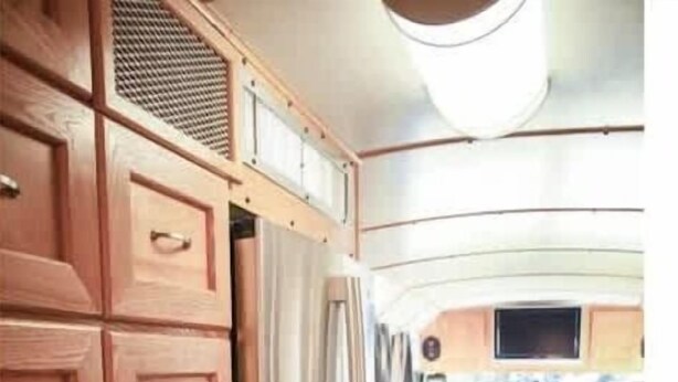 Un intérieur de camping-car compact comprenant un coin cuisine, un espace salon avec un canapé et un téléviseur, ainsi qu’une petite table à manger.