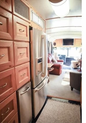 Un intérieur de camping-car compact comprenant un coin cuisine, un espace salon avec un canapé et un téléviseur, ainsi qu’une petite table à manger.