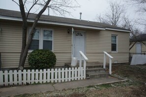 A single-story house with a front porch, a white picket fence, and a small front yard.
