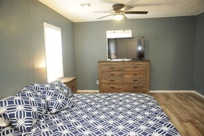 A bedroom with a bed, a dresser, a ceiling fan, and a window.