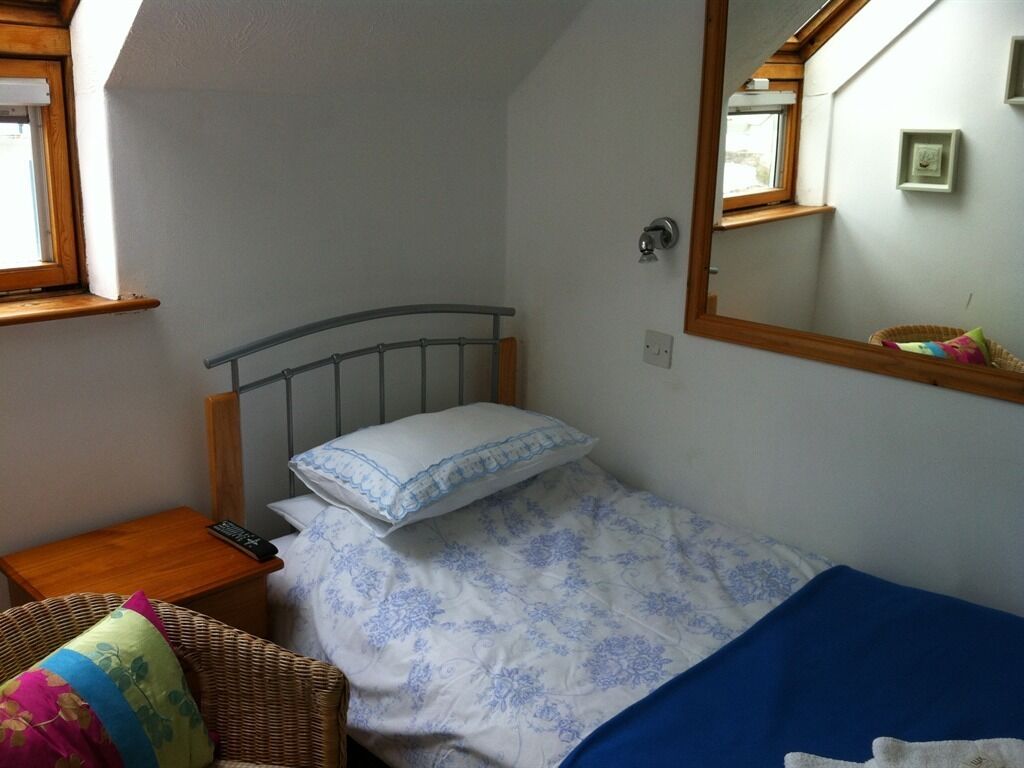 Une chambre à coucher avec un lit, une table de chevet, une chaise en osier, un miroir et une fenêtre.