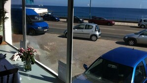 A view from inside a building with a large window overlooking a street with parked cars and a body of water in the distance. - The Stanley (Penzance)