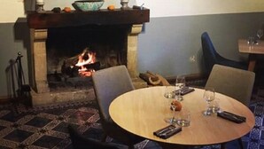 A dining area with a fireplace, a round wooden table, and patterned floor tiles. - Le Cheval Blanc (La Bastide-des-Jourdans)
