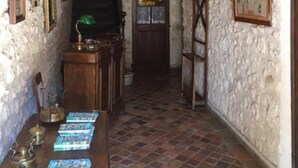 A narrow hallway with stone walls, a wooden door, and a tiled floor. There is a table with books and a lamp in the foreground. - Le Cheval Blanc (La Bastide-des-Jourdans)