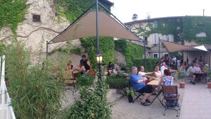 An outdoor dining area with tables and chairs, surrounded by greenery and a building with ivy-covered walls. - Le Cheval Blanc (La Bastide-des-Jourdans)